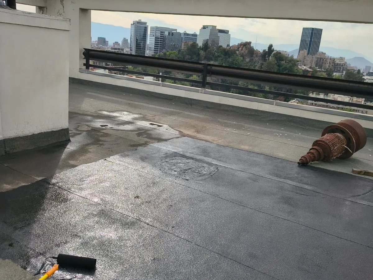 Imprimante asfáltico aplicado con rodillo sobre la azotea de un edificio, con el pretil de fondo