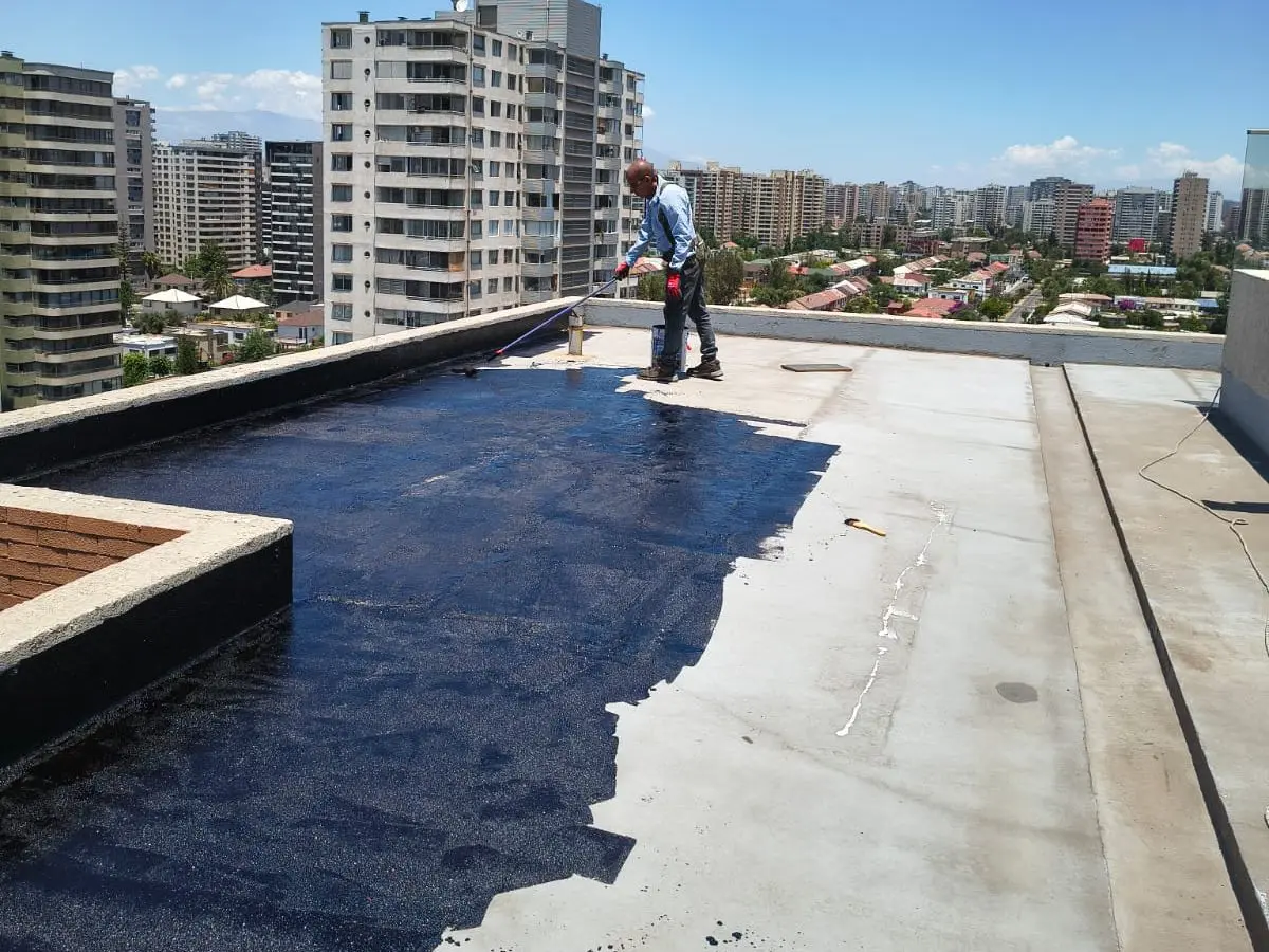 Especialista aplicando la capa asfáltica negra sobre la azotea limpia de un edificio de departamentos