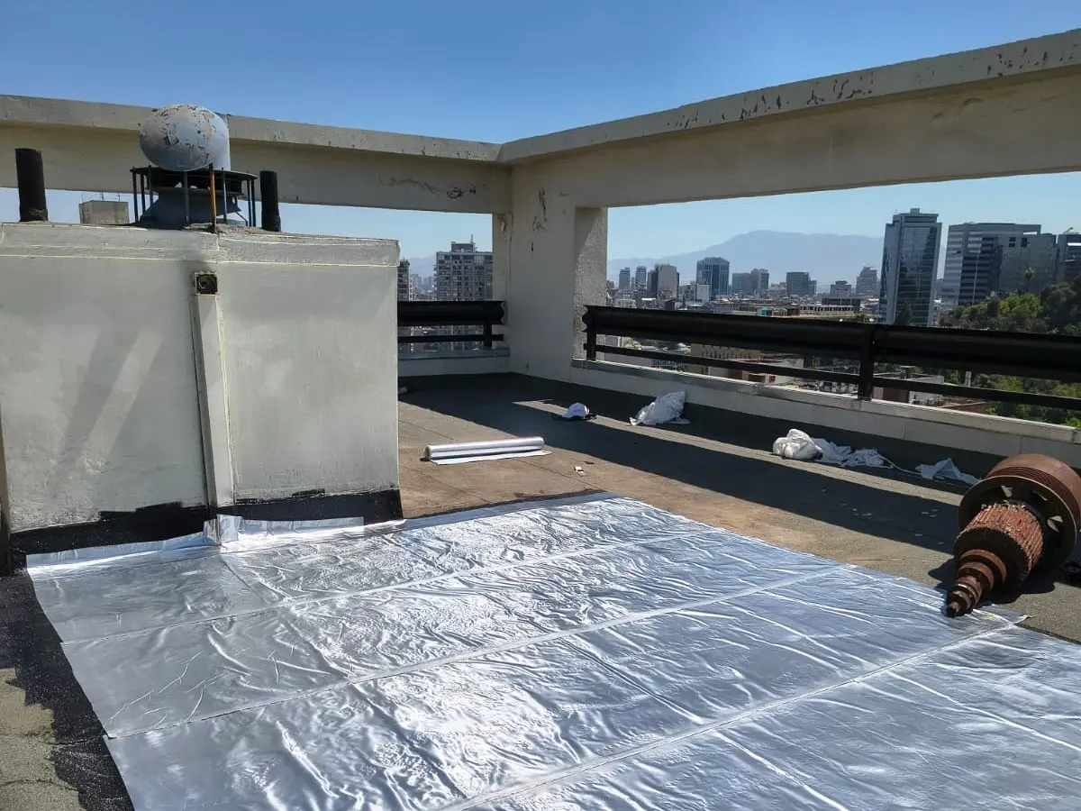 Membrana asfáltica con terminación de aluminio recién instalada en la azotea de un edificio, con la ciudad de fondo